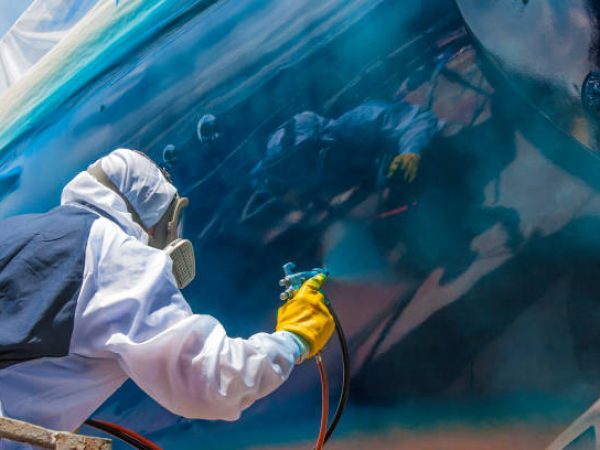 Whangarei, New Zealand, 11-30-2018, worker in full body protection suit and mask is spray painting the hull of a sailing yacht as final work of corrosion protection